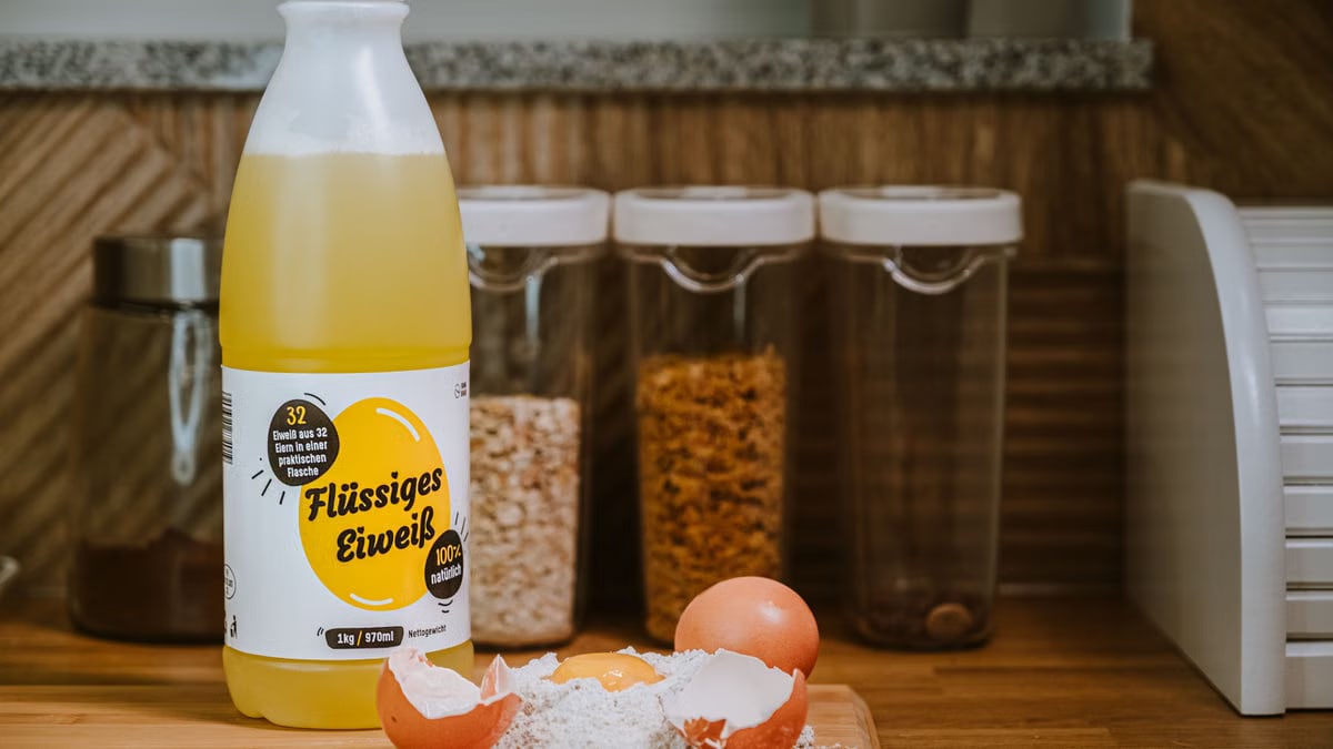 Liquid egg product bottle with cracked eggs and flour on kitchen counter.