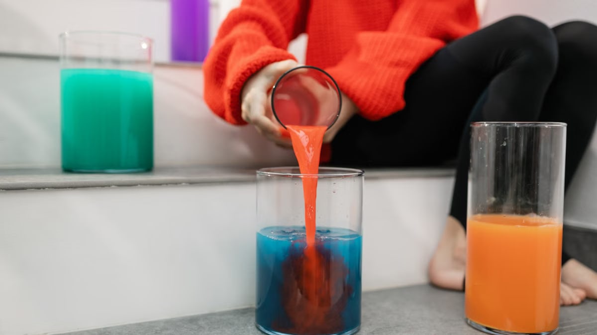 A person pouring vibrant colored liquid into a glass on indoor steps.